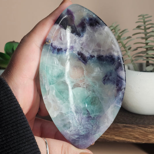 Front view of the marquise-shaped Fluorite bowl held in hand, showcasing its elongated oval form and natural zoning of white, purple, blue, and green with a polished finish.