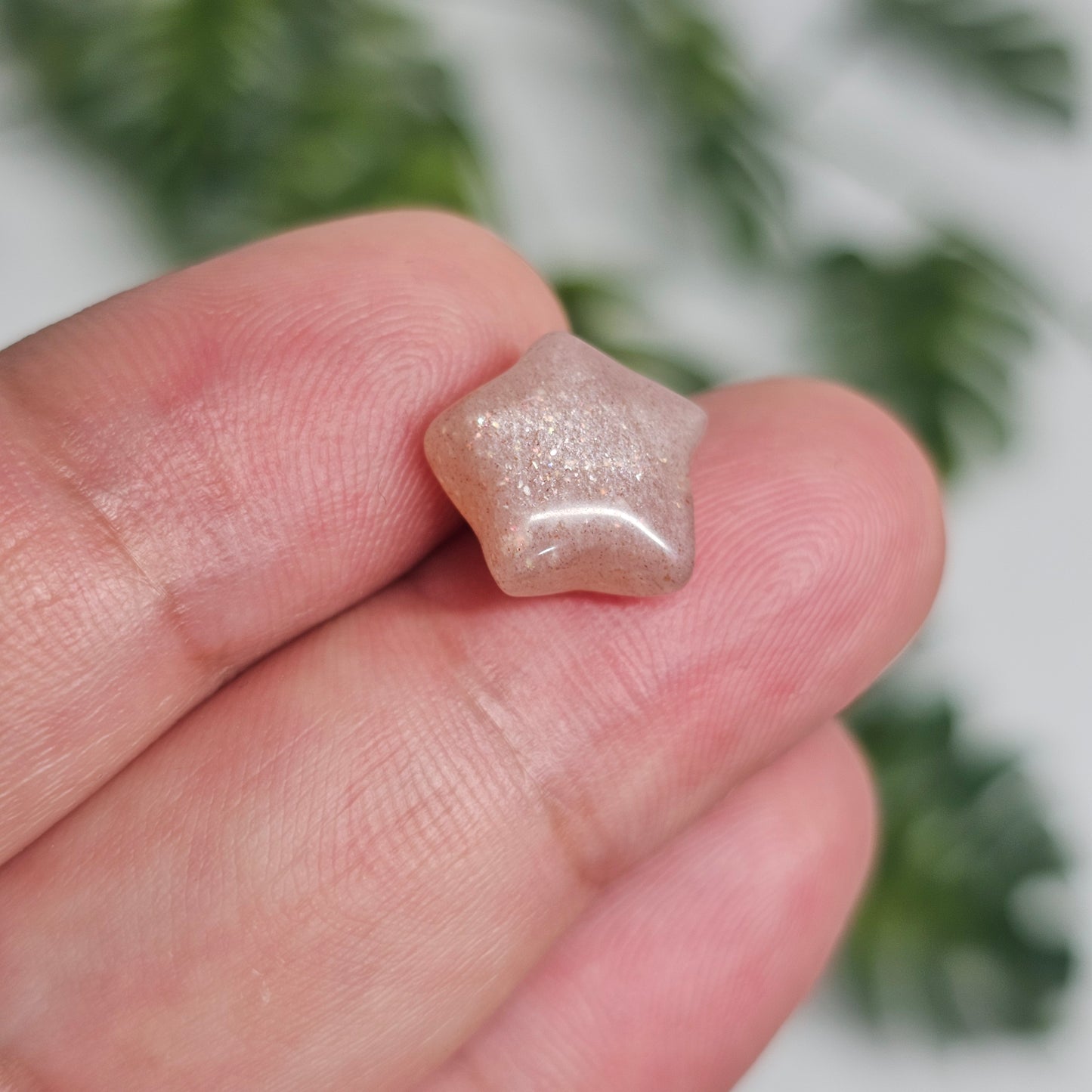In-hand view of the Mini Sunstone star highlighting its delicate carving, shimmering reflective inclusions, and soft warm tones under natural lighting.