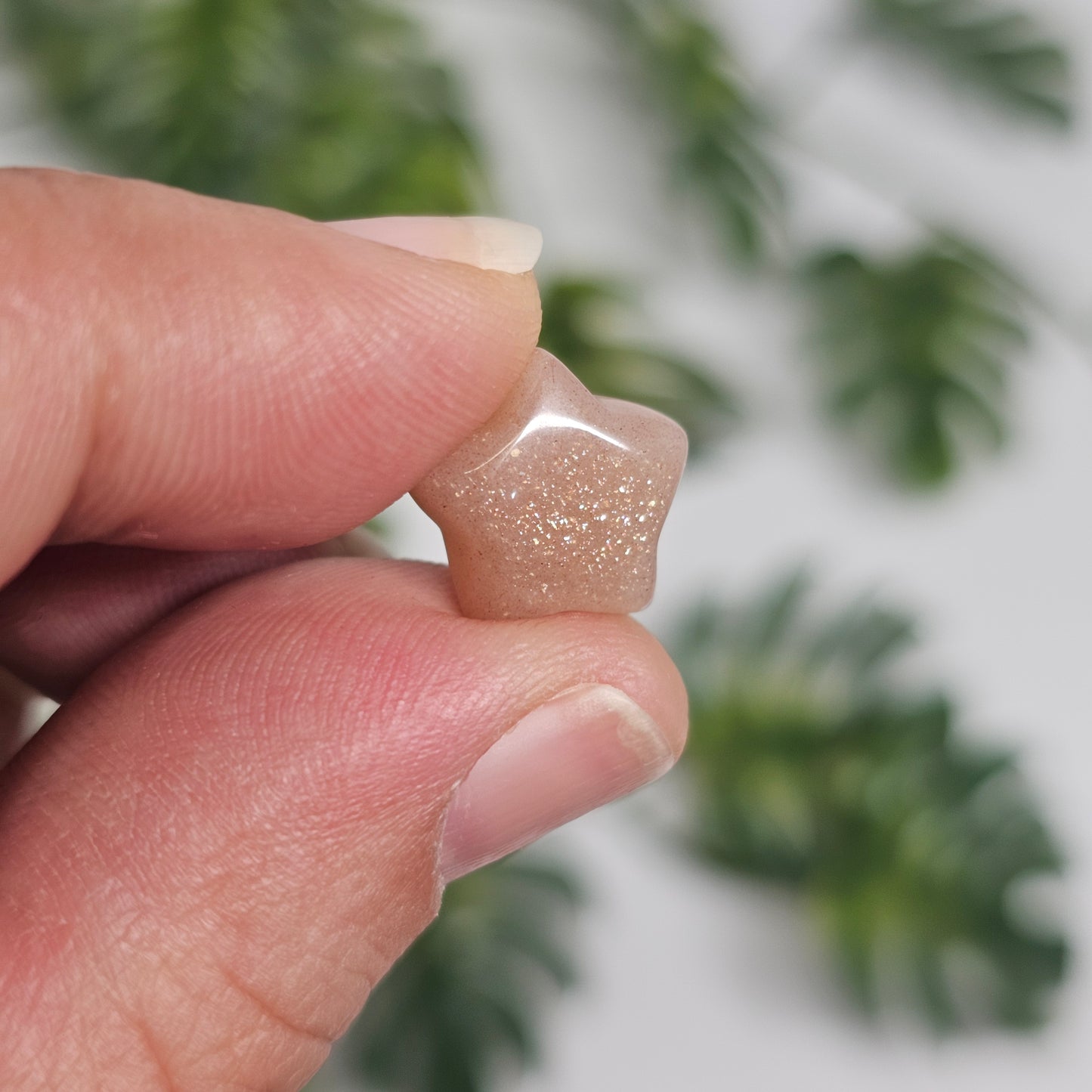 Mini Sunstone star held in hand for size reference, showcasing its warm peachy-orange colouring, polished finish, and natural glittery aventurescence that sparkles beautifully in the light.