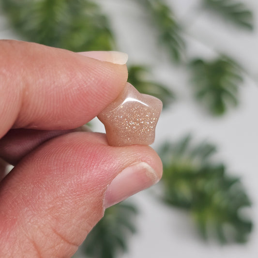 Mini Sunstone star held in hand for size reference, showcasing its warm peachy-orange colouring, polished finish, and natural glittery aventurescence that sparkles beautifully in the light.