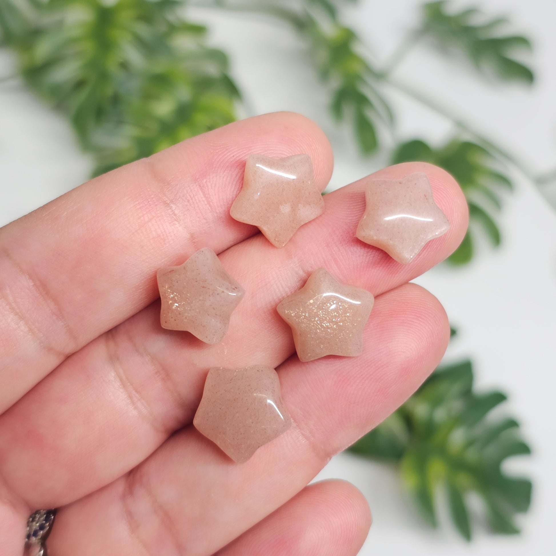 Multiple Mini Sunstone star carvings splayed across the hand, showcasing their petite size, polished star shapes, warm peachy-orange tones, and sparkling aventurescence visible throughout the collection.