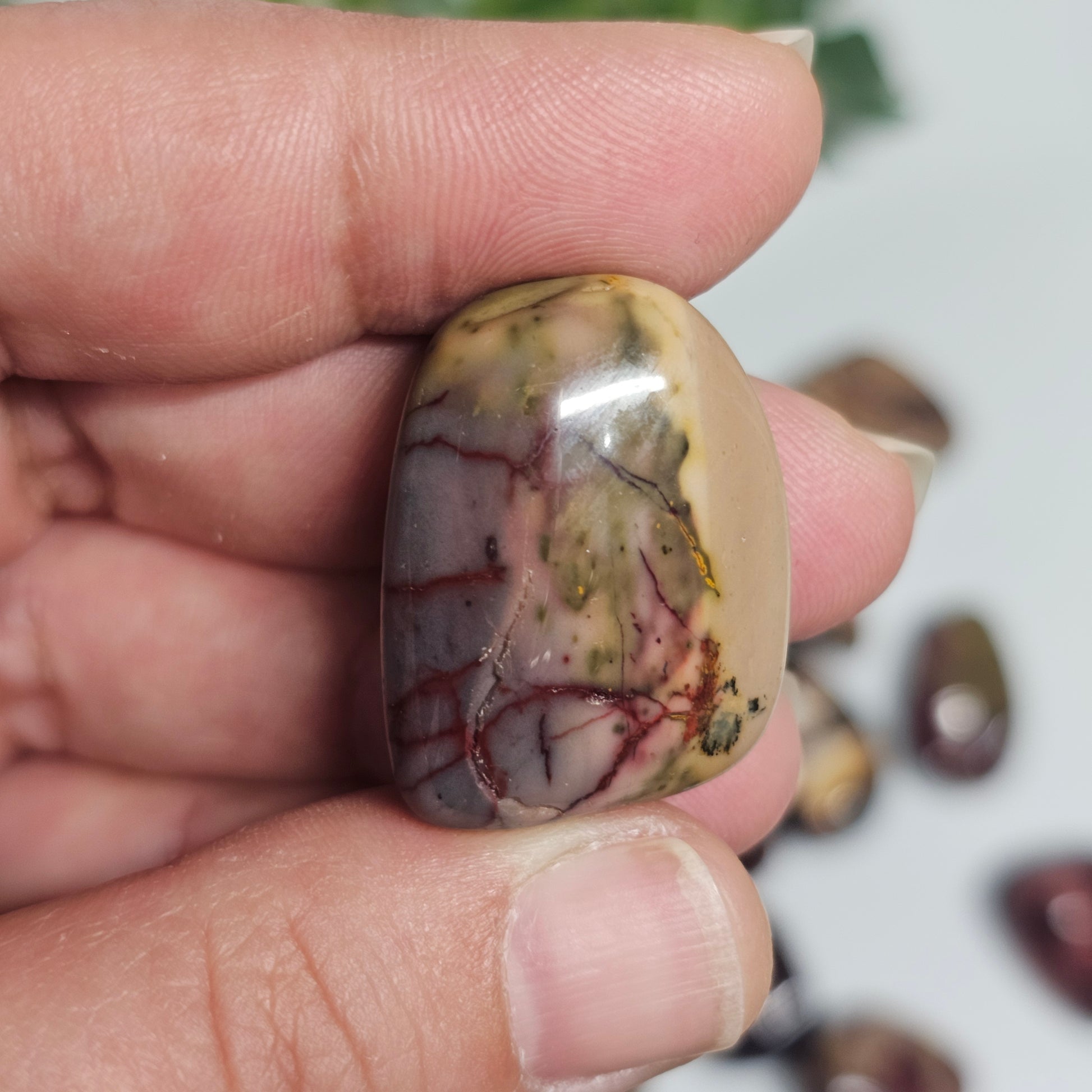 Close-up in-hand view of a Mookaite Jasper tumble stone, highlighting its earthy patterns and grounding natural colouring.