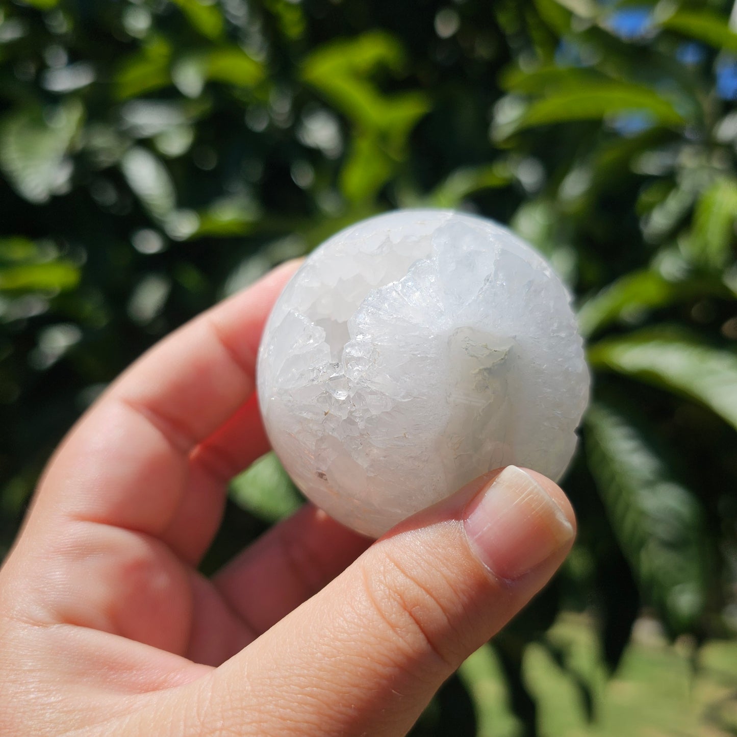 Outdoor in-hand angle showing the sphere’s natural moss patterns and quartz clarity from a different perspective in natural light.