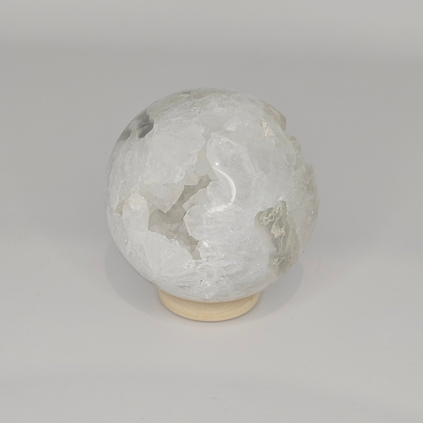 Studio-lit view of the sphere on its stand, showcasing the internal quartz “teeth” formations and suspended moss agate inclusions.