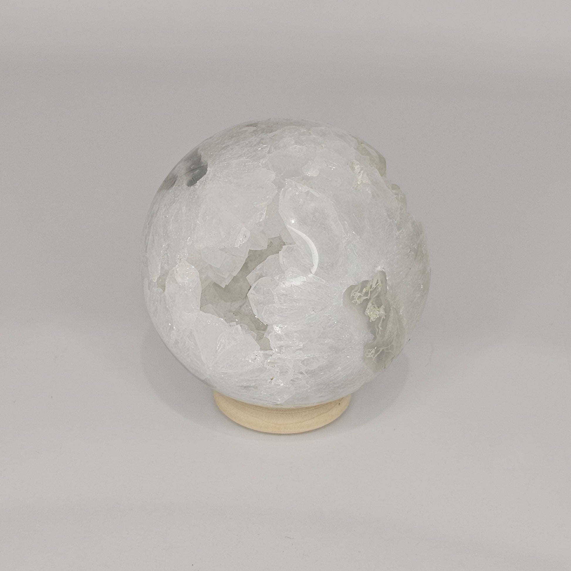 Studio-lit view of the sphere on its stand, showcasing the internal quartz “teeth” formations and suspended moss agate inclusions.