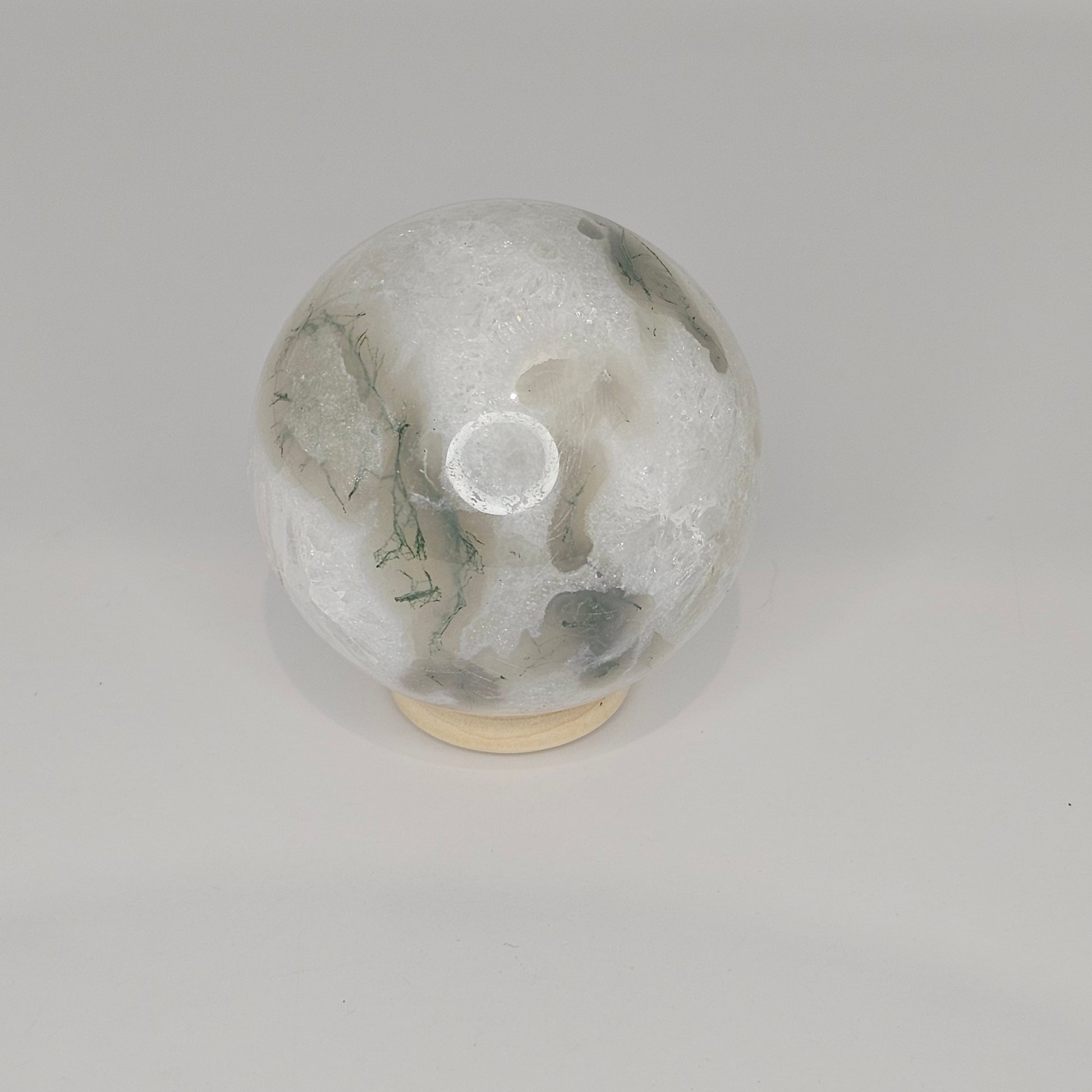 Front display of the Moss Agate Quartz sphere on its stand under studio lighting, showcasing its clear quartz structure, green moss inclusions, and natural crystal formations.