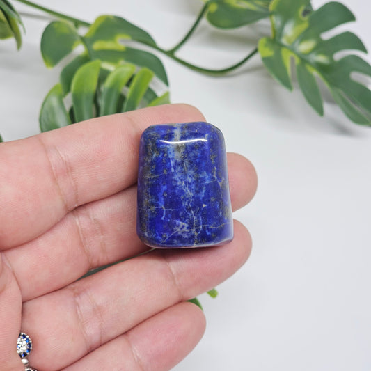 High quality AA Grade Lapis Lazuli polished tumble crystal photographed in hand to show size, colour, and natural Pyrite inclusions. Beautiful deep blue healing stone available in Australia.
