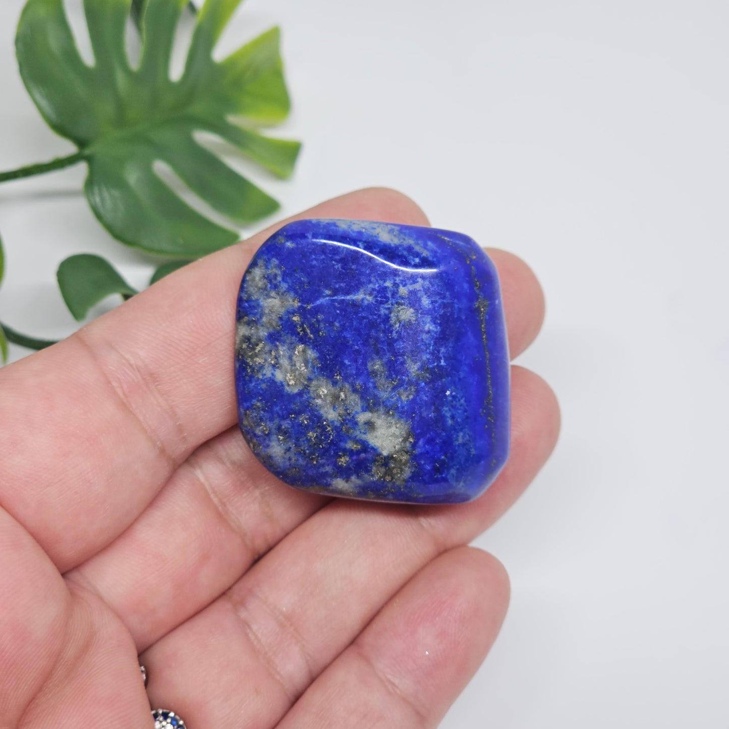 High quality AA Grade Lapis Lazuli polished tumble crystal photographed in hand to show size, colour, and natural Pyrite inclusions. Beautiful deep blue healing stone available in Australia.