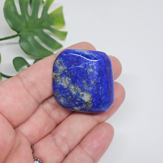 High quality AA Grade Lapis Lazuli polished tumble crystal photographed in hand to show size, colour, and natural Pyrite inclusions. Beautiful deep blue healing stone available in Australia.
