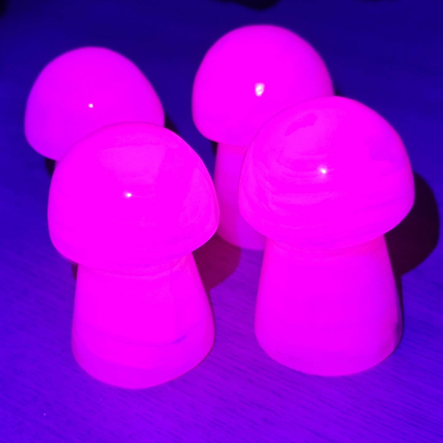 Pink Mangano Calcite mushrooms glowing bright pink under UV light, showcasing strong fluorescence and unique crystal property.