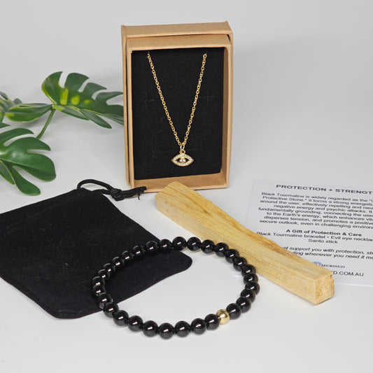 Evil eye necklace in gift box with Black Tourmaline bracelet, Palo Santo stick, velvet pouch and information card styled together.