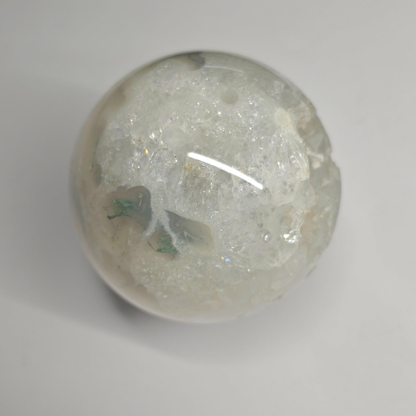 Close-up of the Moss Agate Quartz sphere highlighting natural quartz formations with mini rainbow inclusions, set within earthy green moss agate patterns and clear crystal structure.