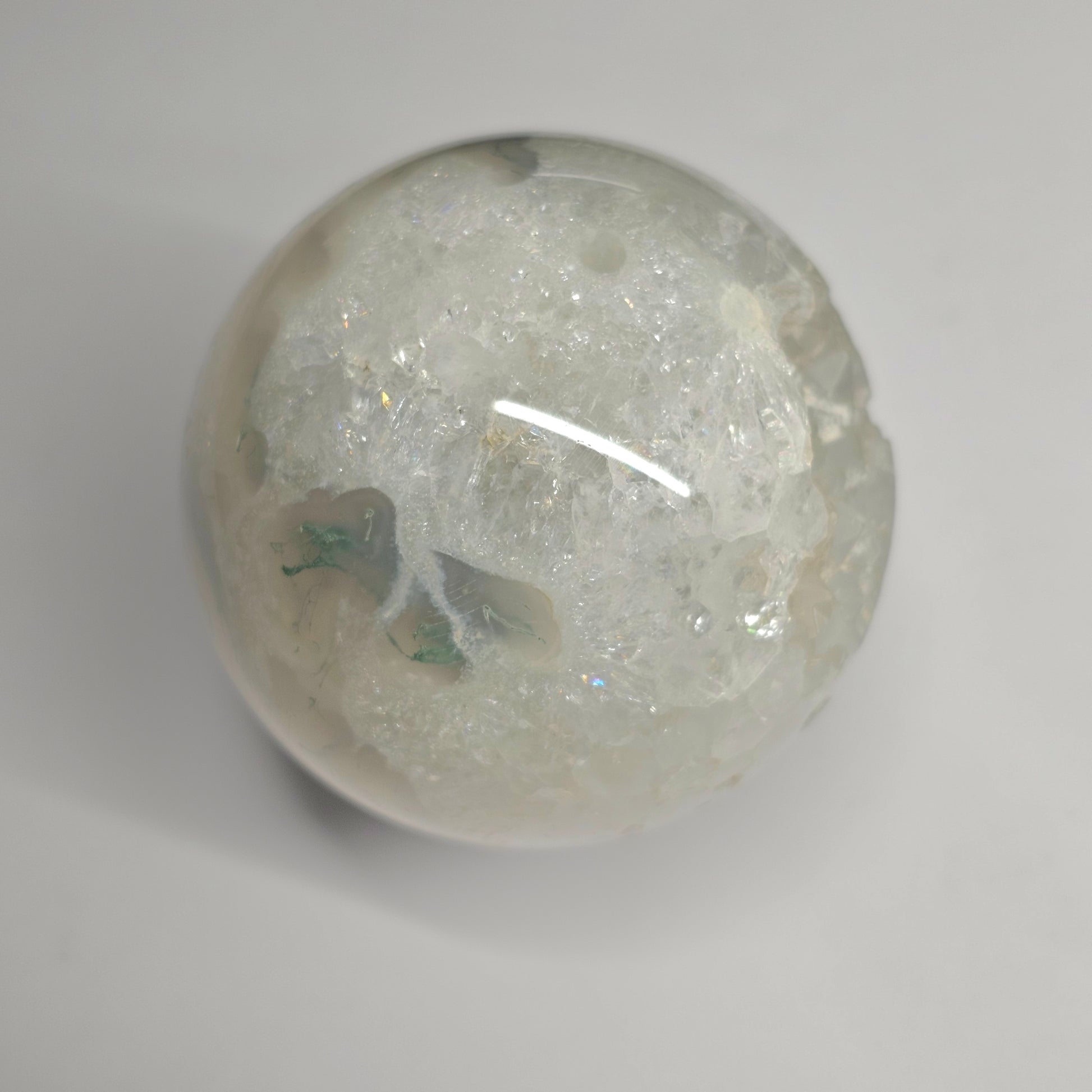 Close-up of the Moss Agate Quartz sphere highlighting natural quartz formations with mini rainbow inclusions, set within earthy green moss agate patterns and clear crystal structure.