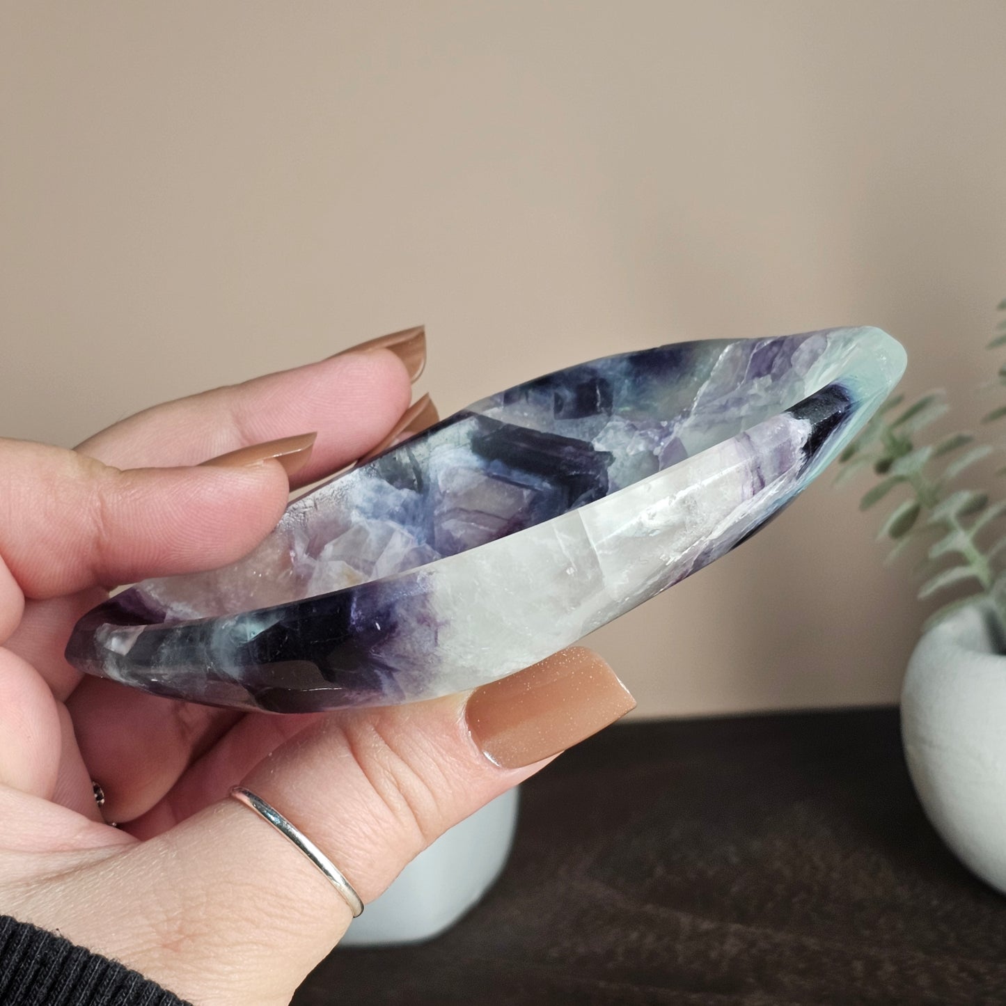 Side profile of the Fluorite dish in hand showing its slim polished edge and natural banding of white, purple, blue, and green tones.