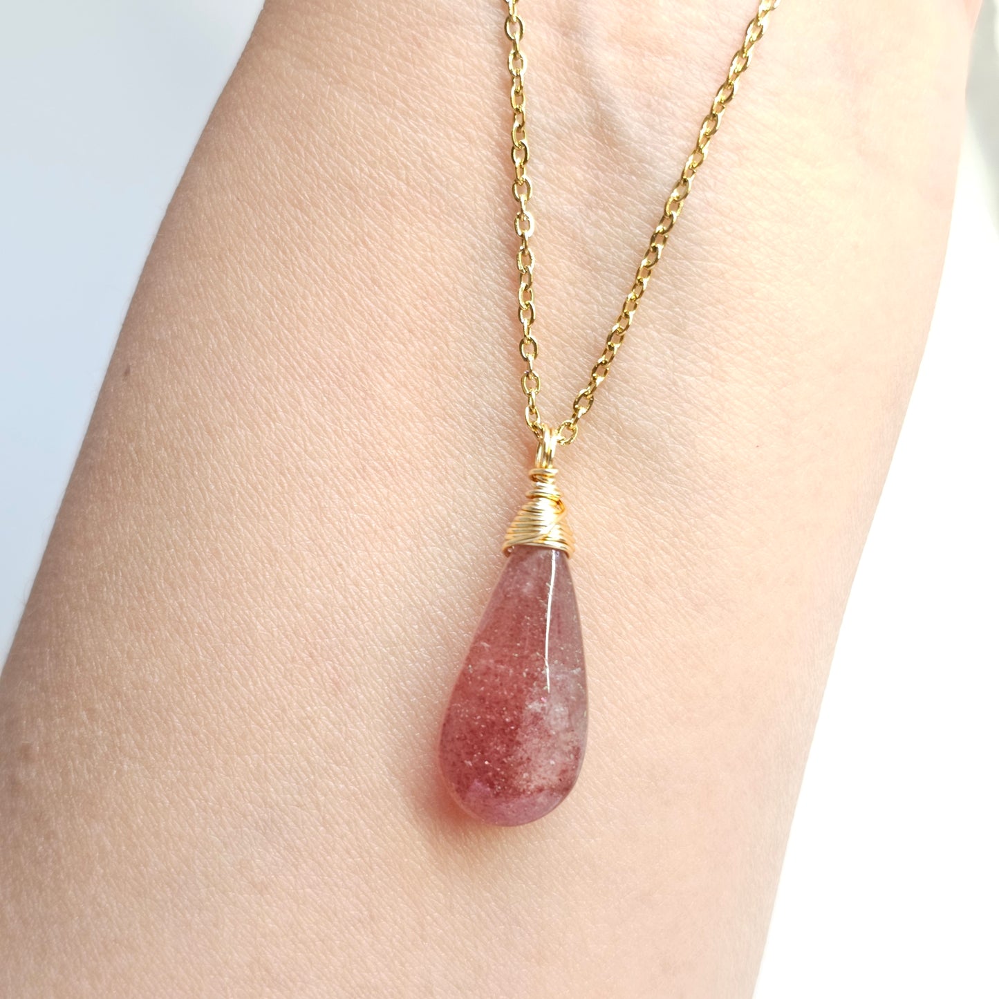 Handmade Red Aventurine pendant with natural shimmer, wire wrapped in gold and suspended from a stainless steel chain. Shown dangling from hand down the arm under studio lights.