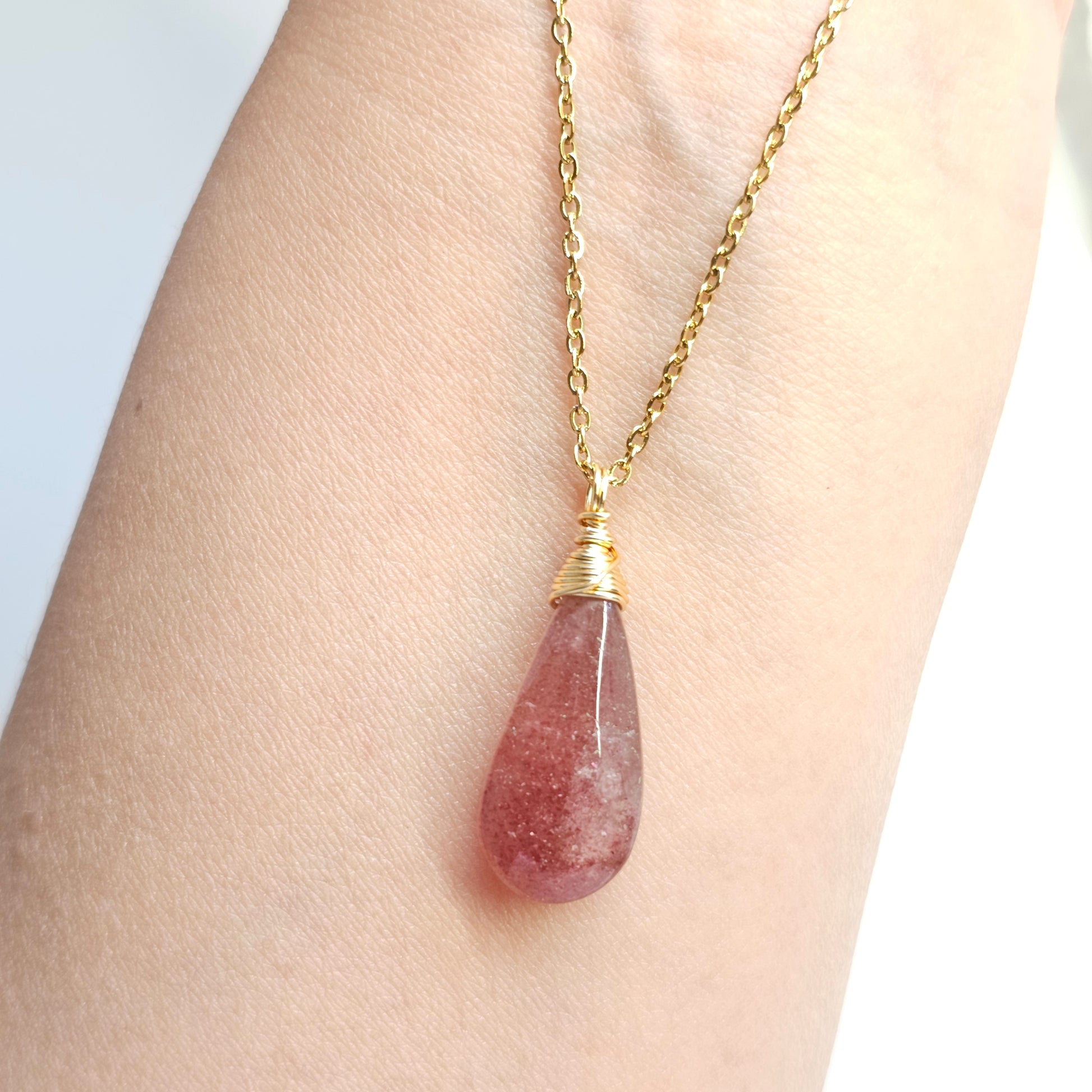 Handmade Red Aventurine pendant with natural shimmer, wire wrapped in gold and suspended from a stainless steel chain. Shown dangling from hand down the arm under studio lights.
