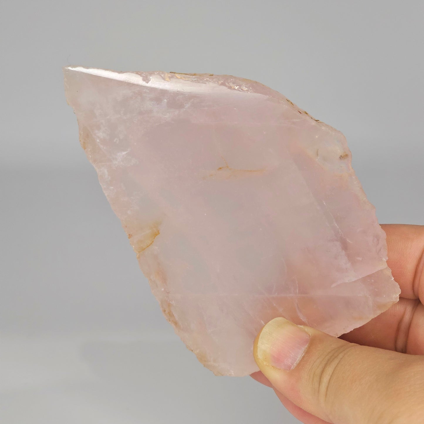 Translucent Rose Quartz slab held in hand under studio lighting, revealing gentle pink tones, polished finish, and internal rainbows.