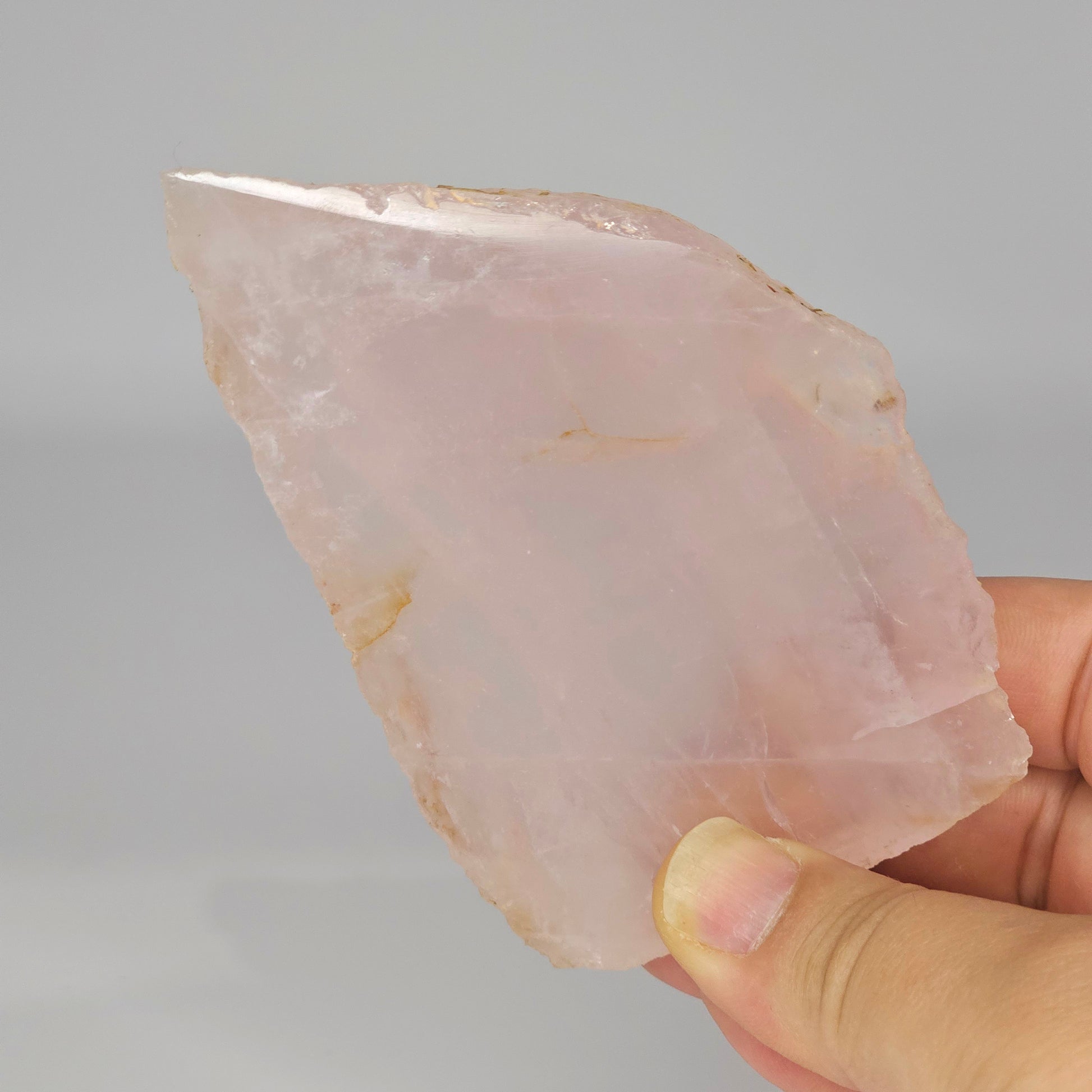 Translucent Rose Quartz slab held in hand under studio lighting, revealing gentle pink tones, polished finish, and internal rainbows.