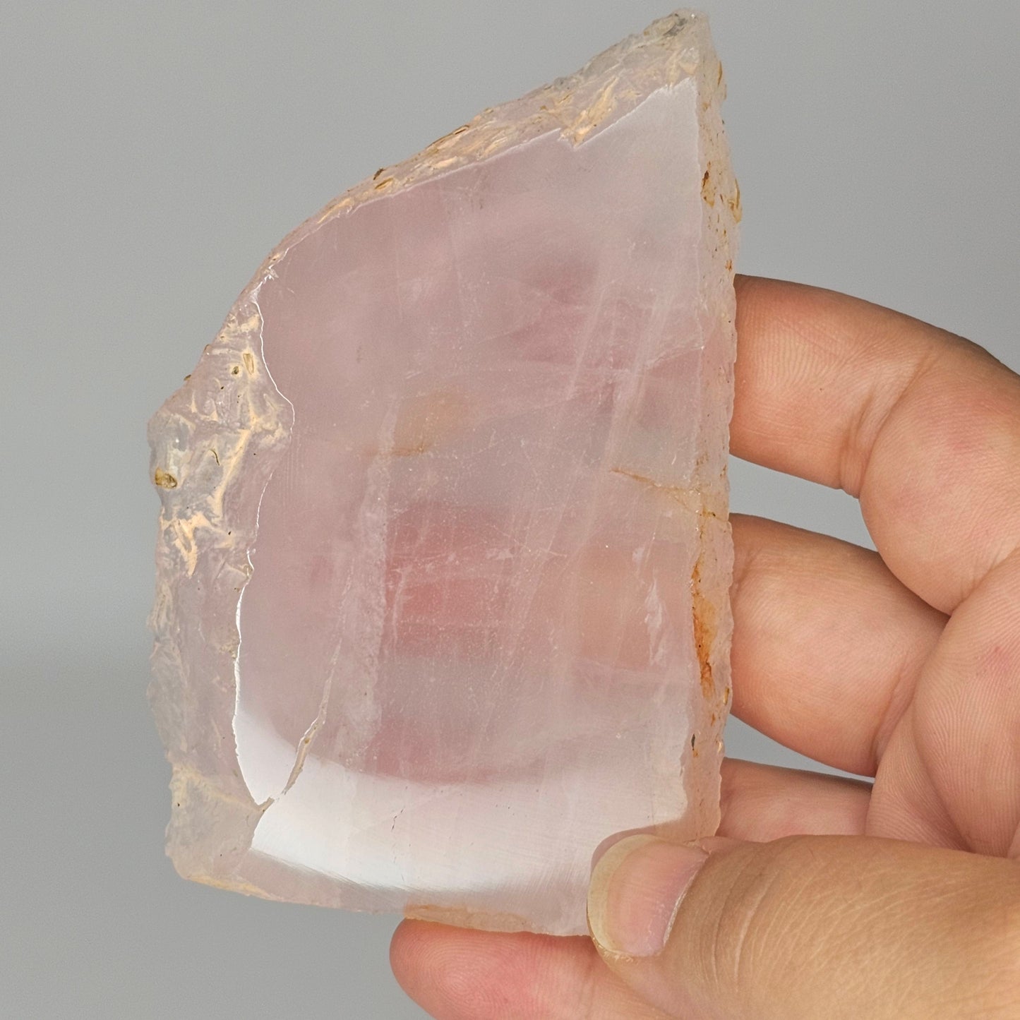 Translucent Rose Quartz slab held in hand under studio lighting, revealing gentle pink tones, polished finish, and internal rainbows.
