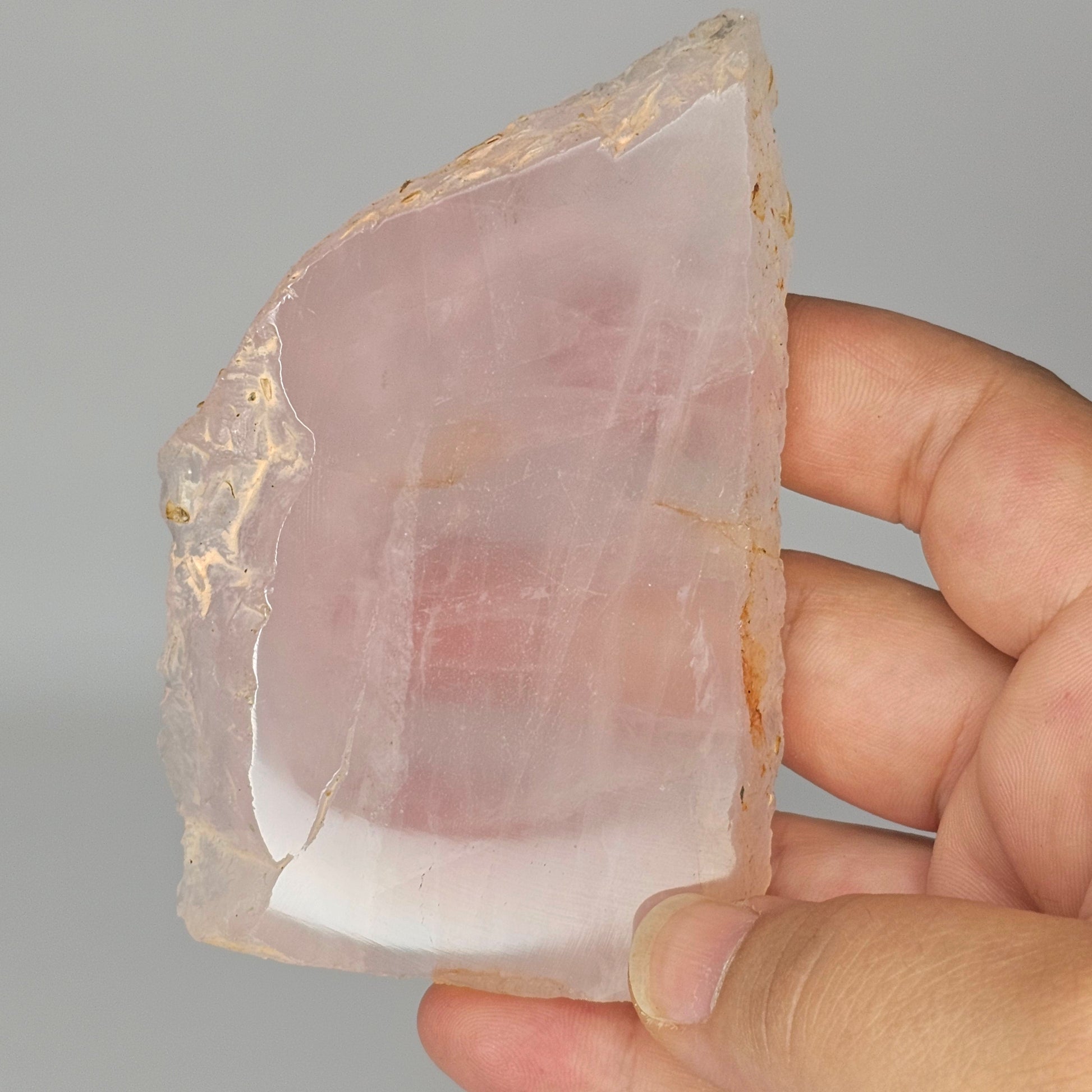 Translucent Rose Quartz slab held in hand under studio lighting, revealing gentle pink tones, polished finish, and internal rainbows.