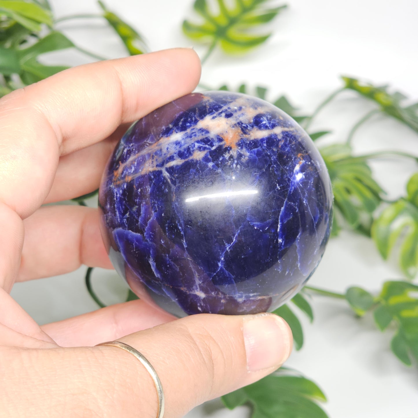 Sodalite crystal sphere A held in hand, showcasing its deep blue tones, white marbling, and smooth polished finish.