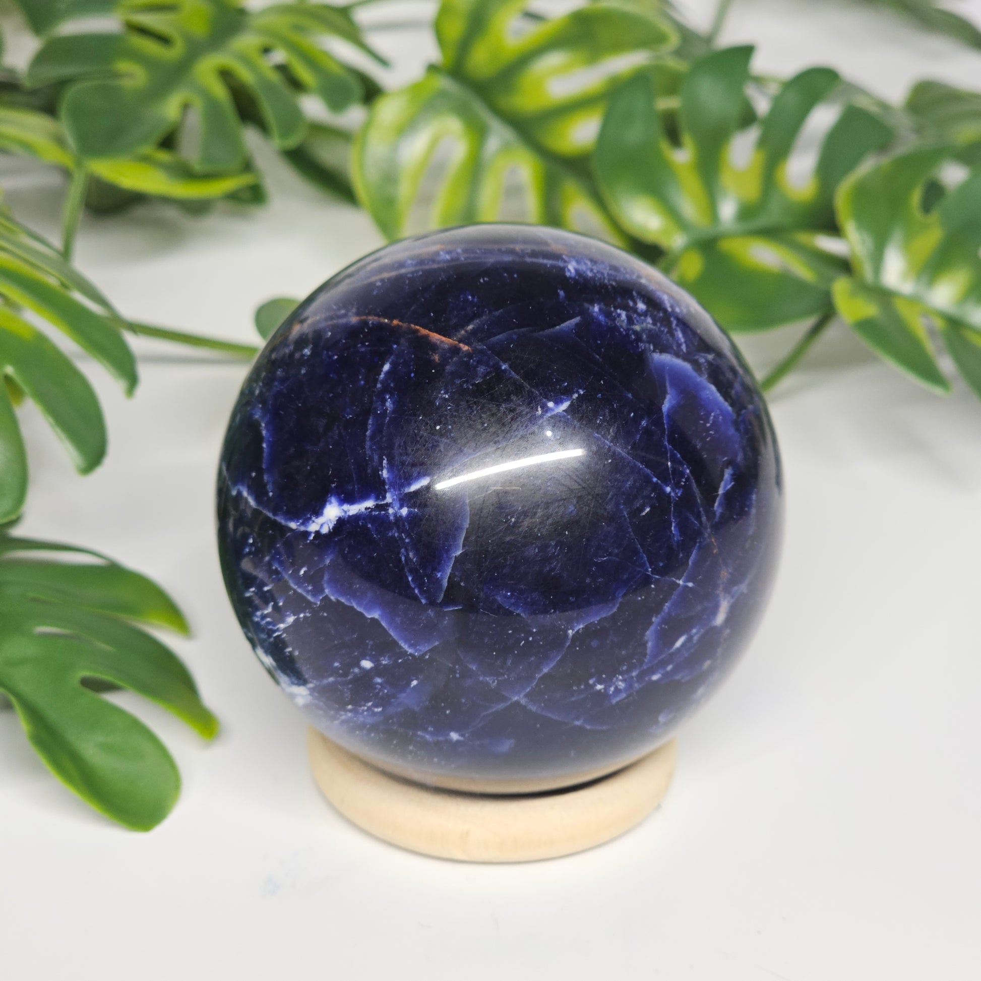 Close-up view of Sodalite sphere A on its stand, highlighting fine white marbling, deep blue tones, and polished crystal surface.