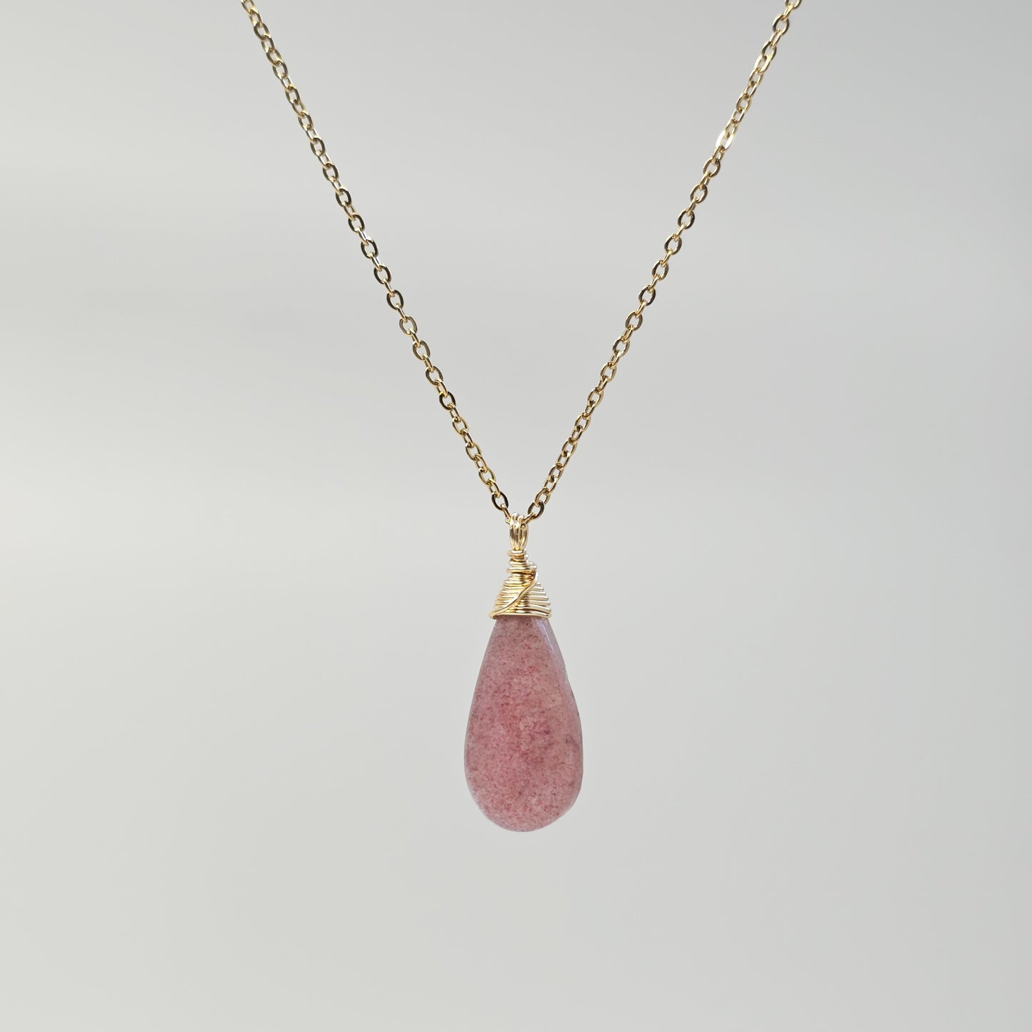 Handmade Red Aventurine pendant with natural shimmer, wire wrapped in gold and suspended from a stainless steel chain. Shown suspended under studio lights.