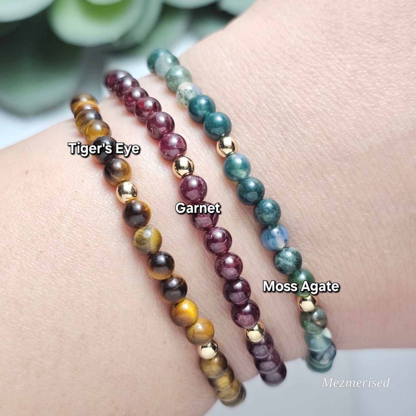 Stacked 4mm Tiger's Eye, Garnet and Moss Agate gemstone bracelets with minimalist gold accent details.