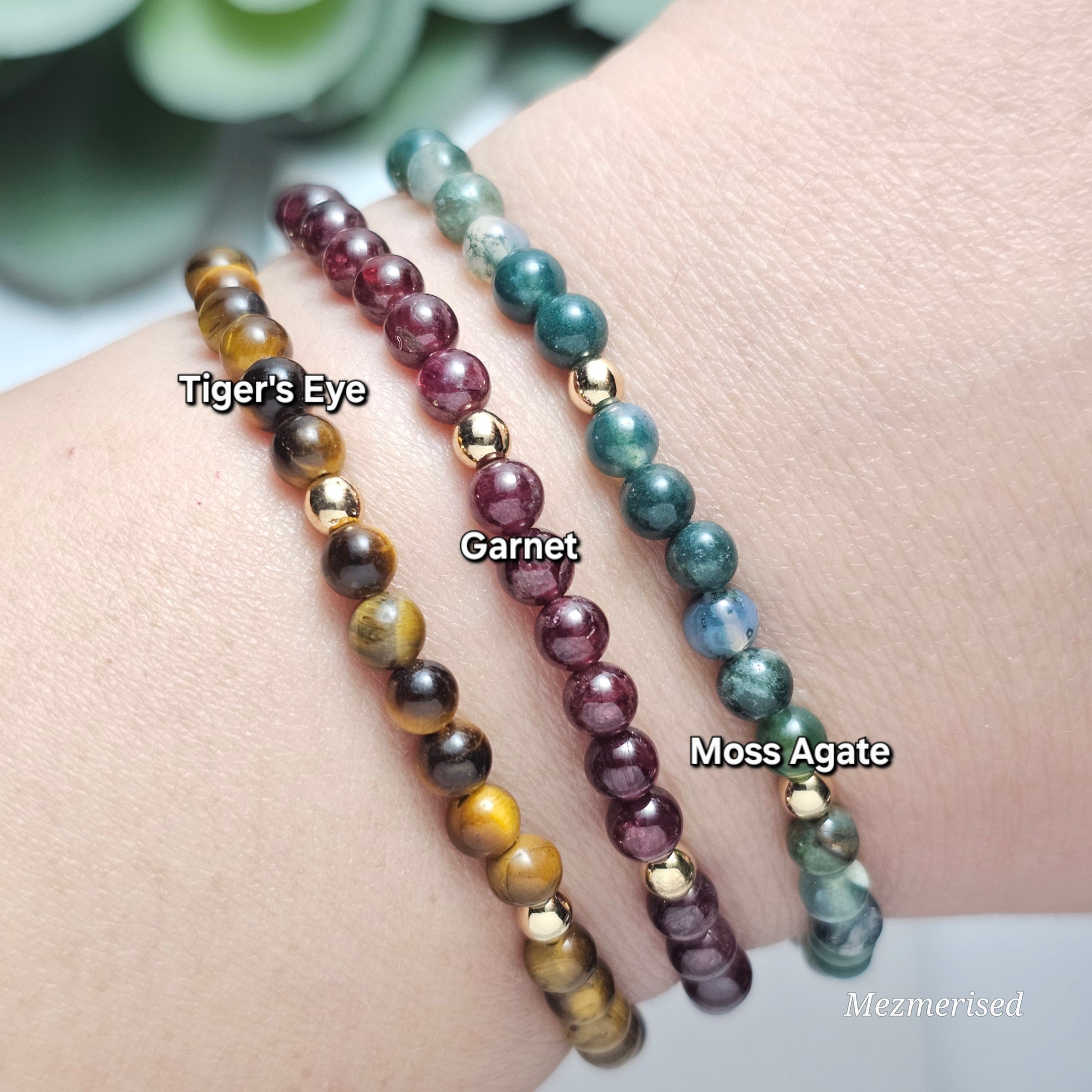 Stacked 4mm Tiger's Eye, Garnet and Moss Agate gemstone bracelets with minimalist gold accent details.