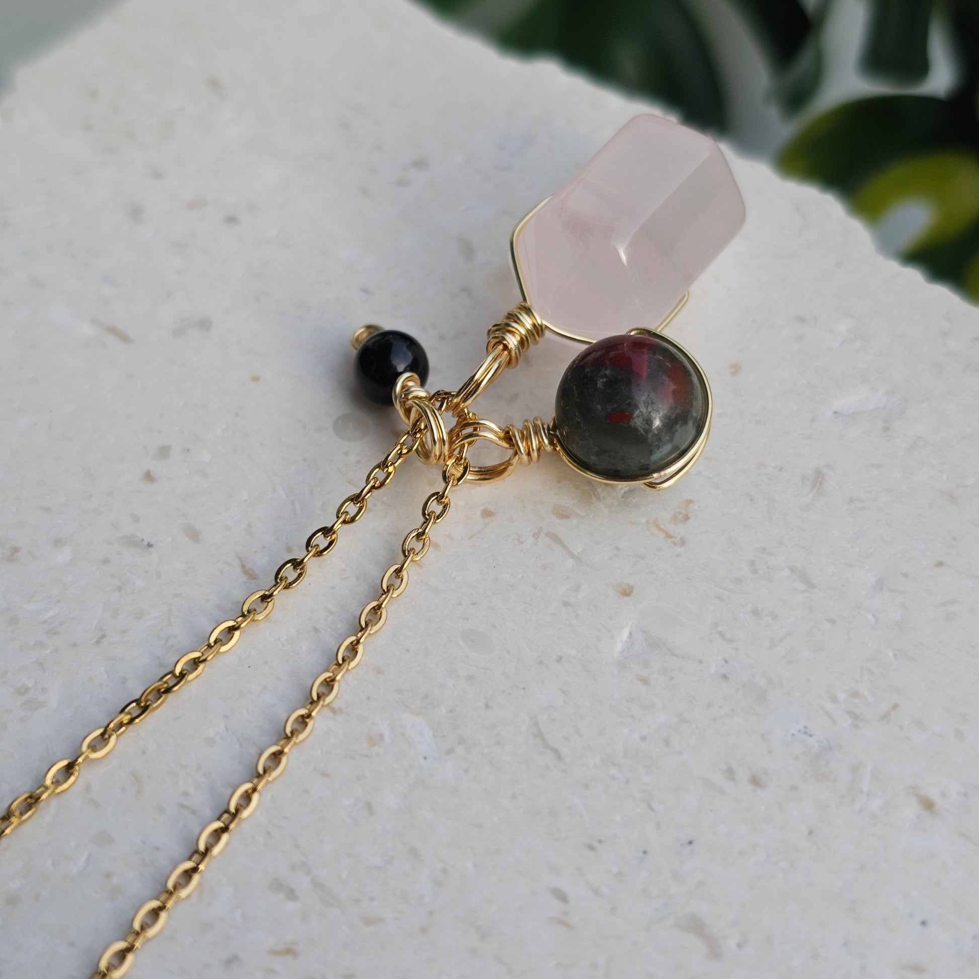 Top view of the Grounded Love Necklace displaying the wire wrapped Rose Quartz double terminated point with Bloodstone Jasper and Black Tourmaline on an 18k gold plated stainless steel chain