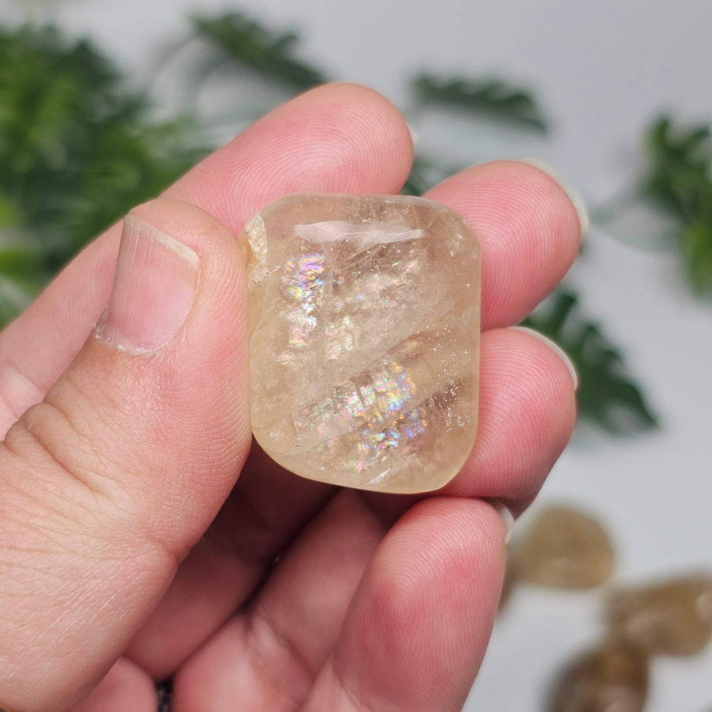 Single Topaz tumble stone held in hand, highlighting its warm golden colour, natural clarity, and polished finish in soft natural light.