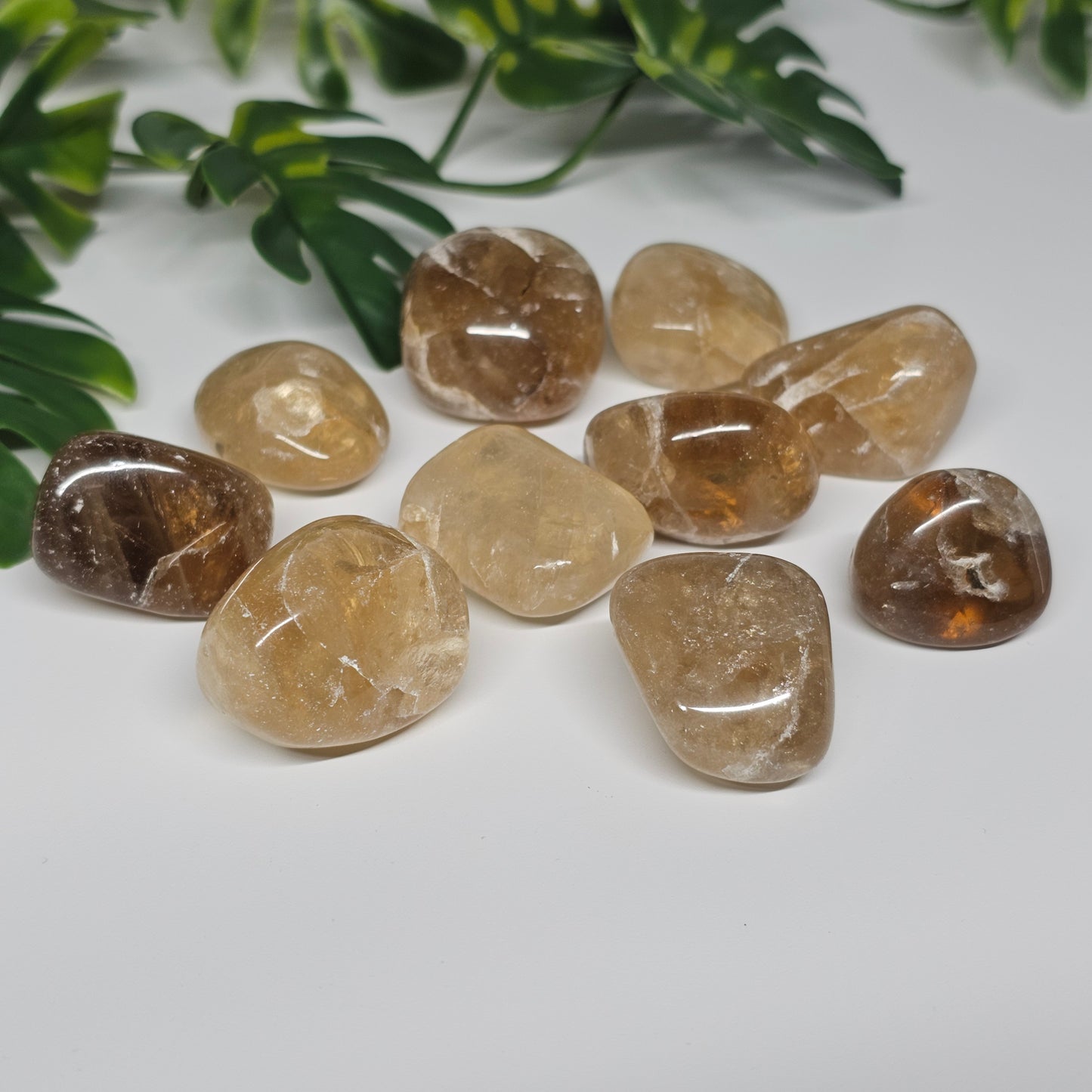 Topaz tumble stones arranged on a flat surface, showcasing a mix of warm golden and yellow-tinged hues with natural translucence and polished finishes.
