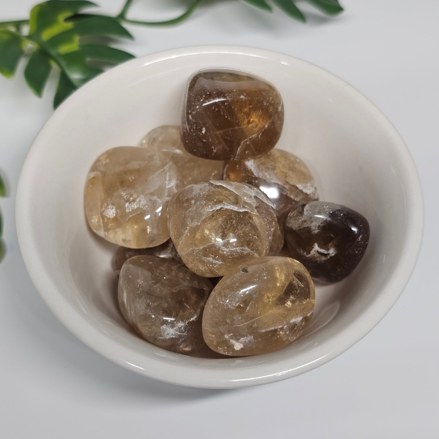 A collection of Topaz tumble stones displayed in a bowl, showcasing natural golden and yellow-tinged hues with soft translucence and polished surfaces.