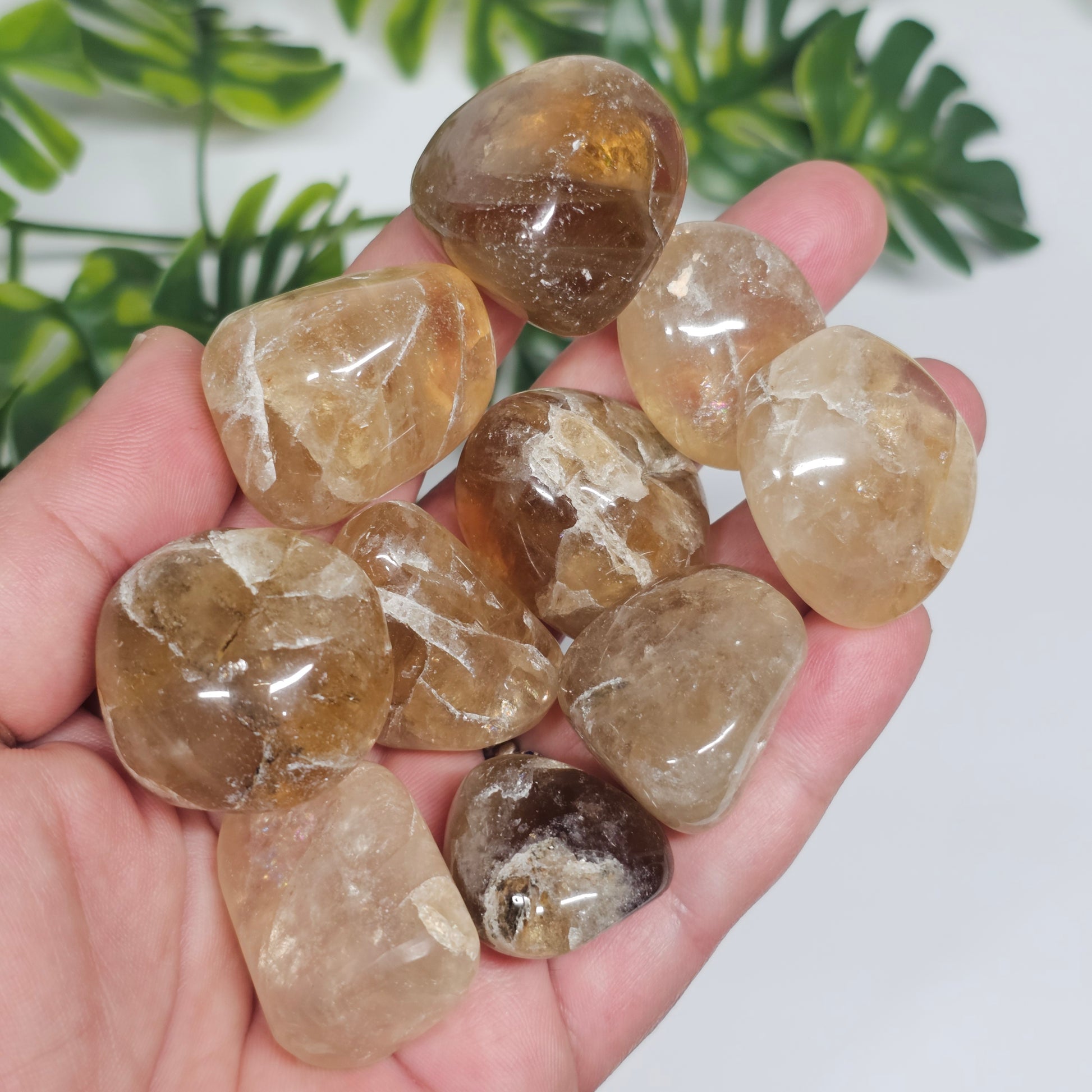 Multiple Topaz tumble stones held in hand for size reference, showing their smooth polished surfaces and warm golden-yellow hues.