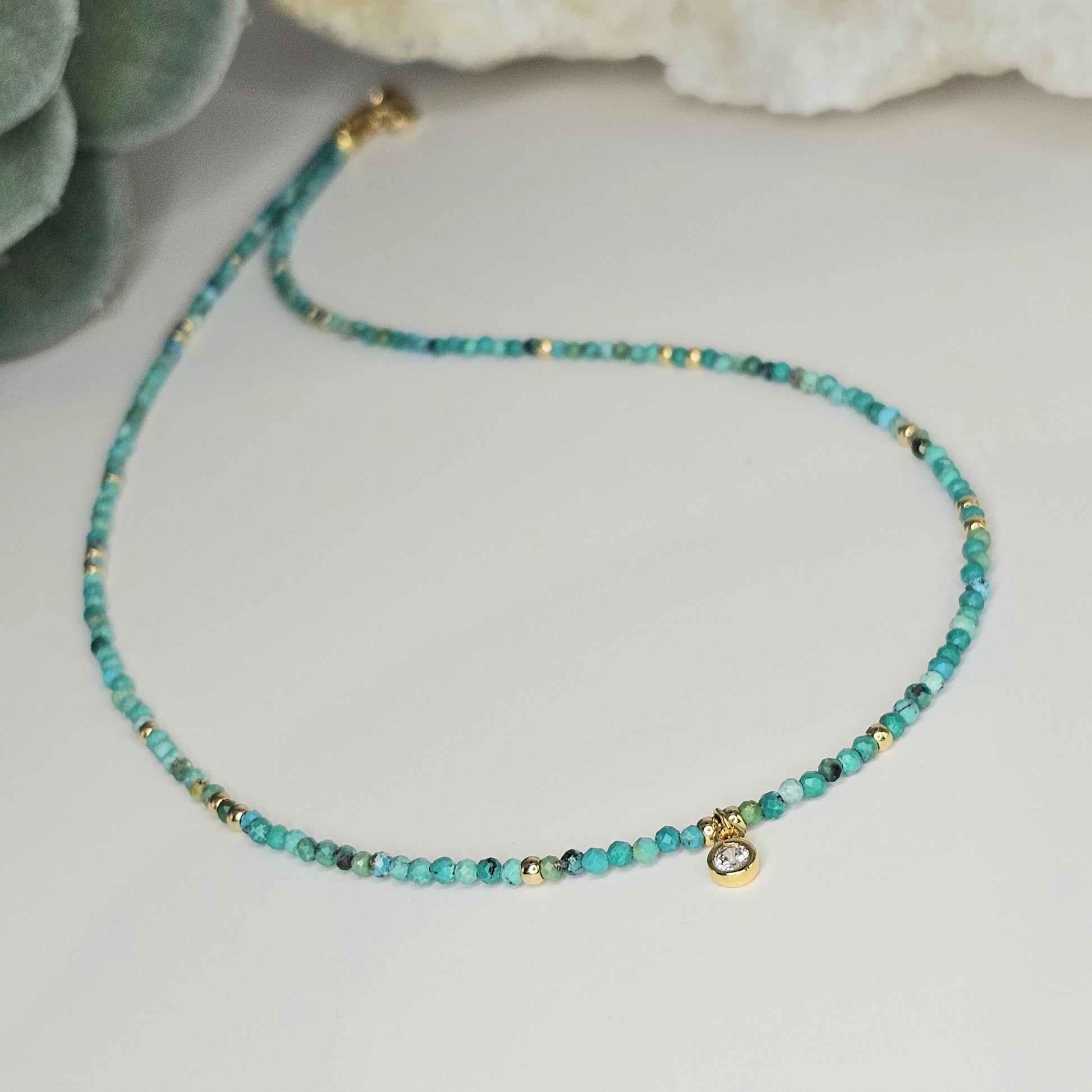 Angled perspective of the full necklace showing the flow of faceted Turquoise beads, gold-toned accents, and the central CZ round pendant.
