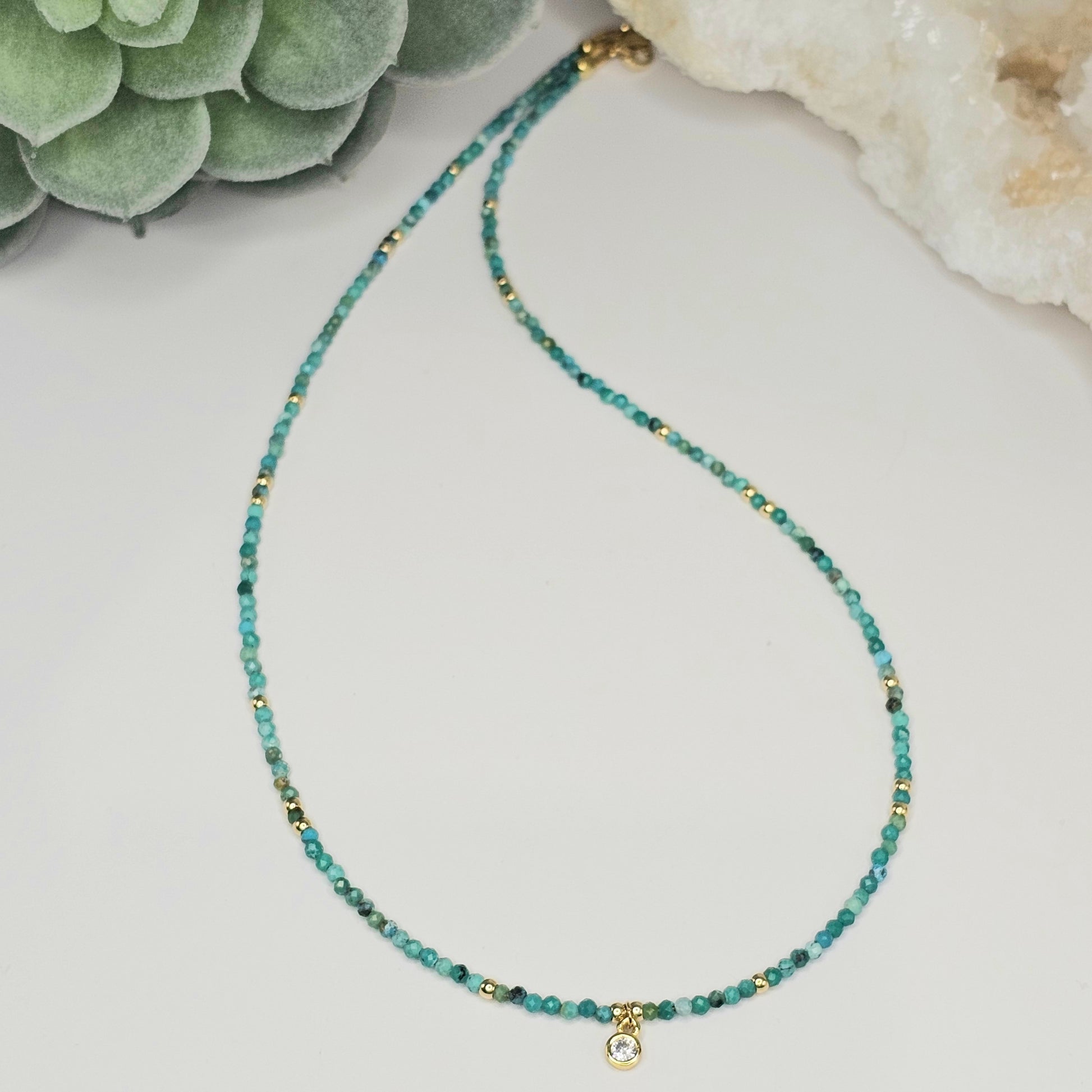 Flat lay view of the 2mm faceted Turquoise bead necklace featuring a CZ round pendant and gold-toned accents, showcasing the full length and balanced design of the piece.
