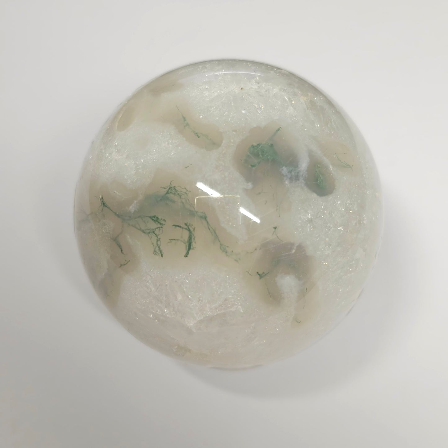 Moss Agate in Quartz sphere under lights, showcasing its clear quartz structure, green moss inclusions, and natural crystal formations.