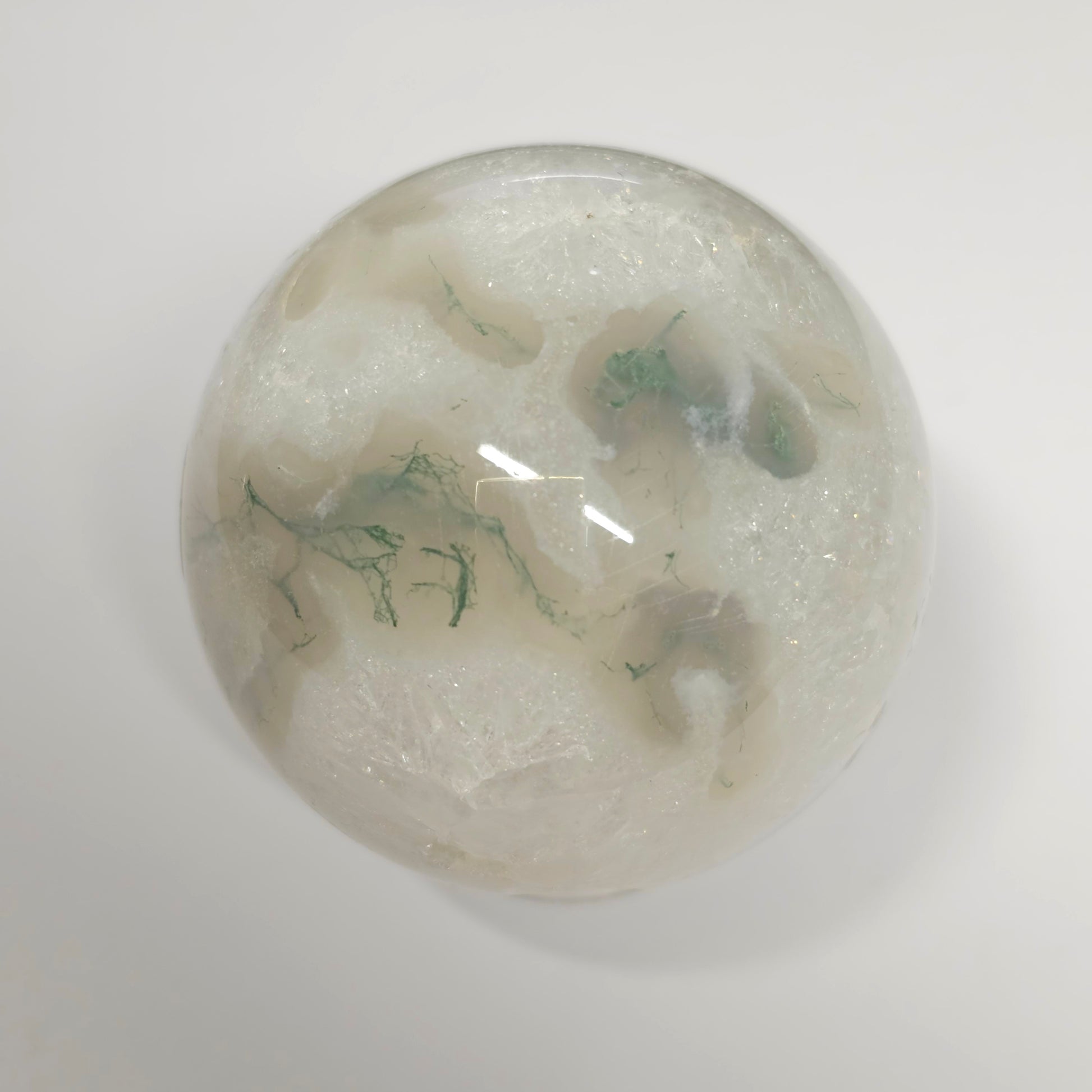 Moss Agate in Quartz sphere under lights, showcasing its clear quartz structure, green moss inclusions, and natural crystal formations.