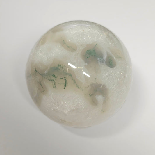 Moss Agate in Quartz sphere under lights, showcasing its clear quartz structure, green moss inclusions, and natural crystal formations.