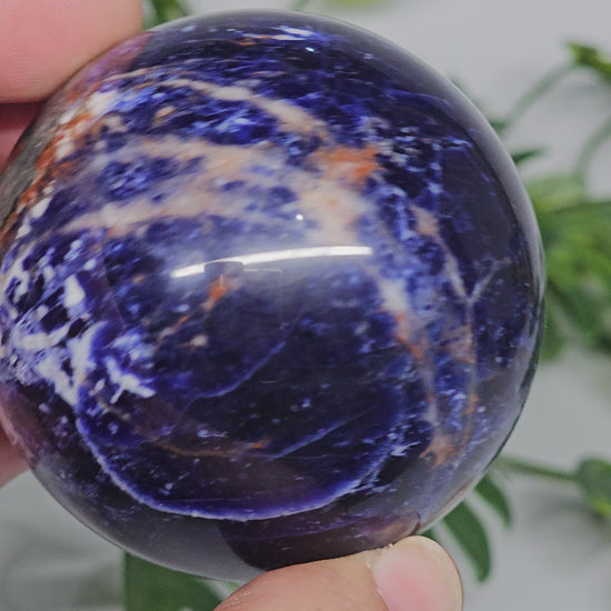 Close-up view of Sodalite sphere A in hand, highlighting fine white marbling, deep blue tones, and polished crystal surface.