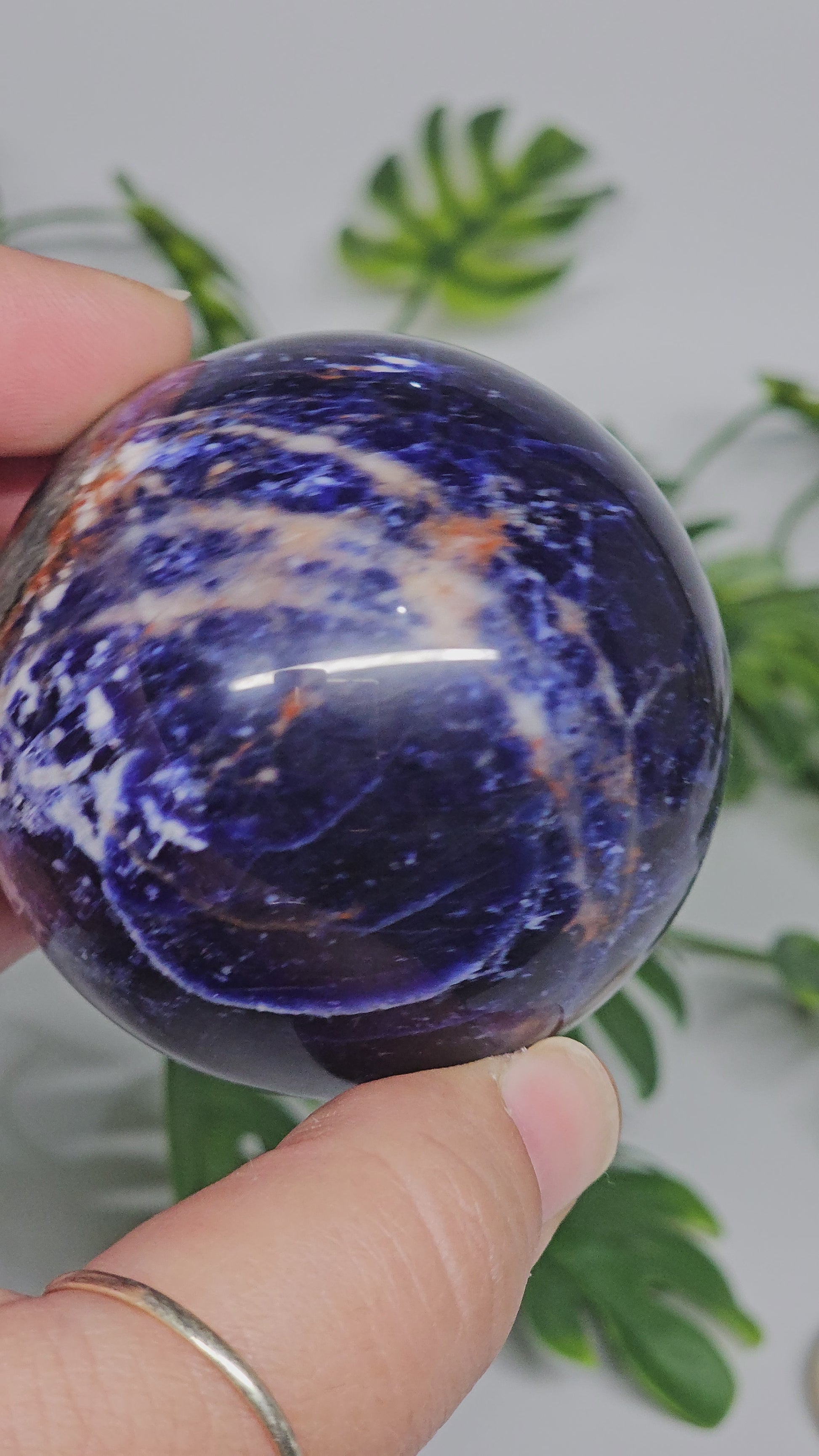 Close-up view of Sodalite sphere A in hand, highlighting fine white marbling, deep blue tones, and polished crystal surface.