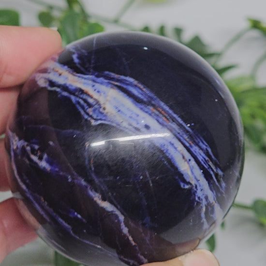 Close-up view of Sodalite sphere B in hand, showing its rich navy blue tones, soft grey marbling, and smooth polished finish.