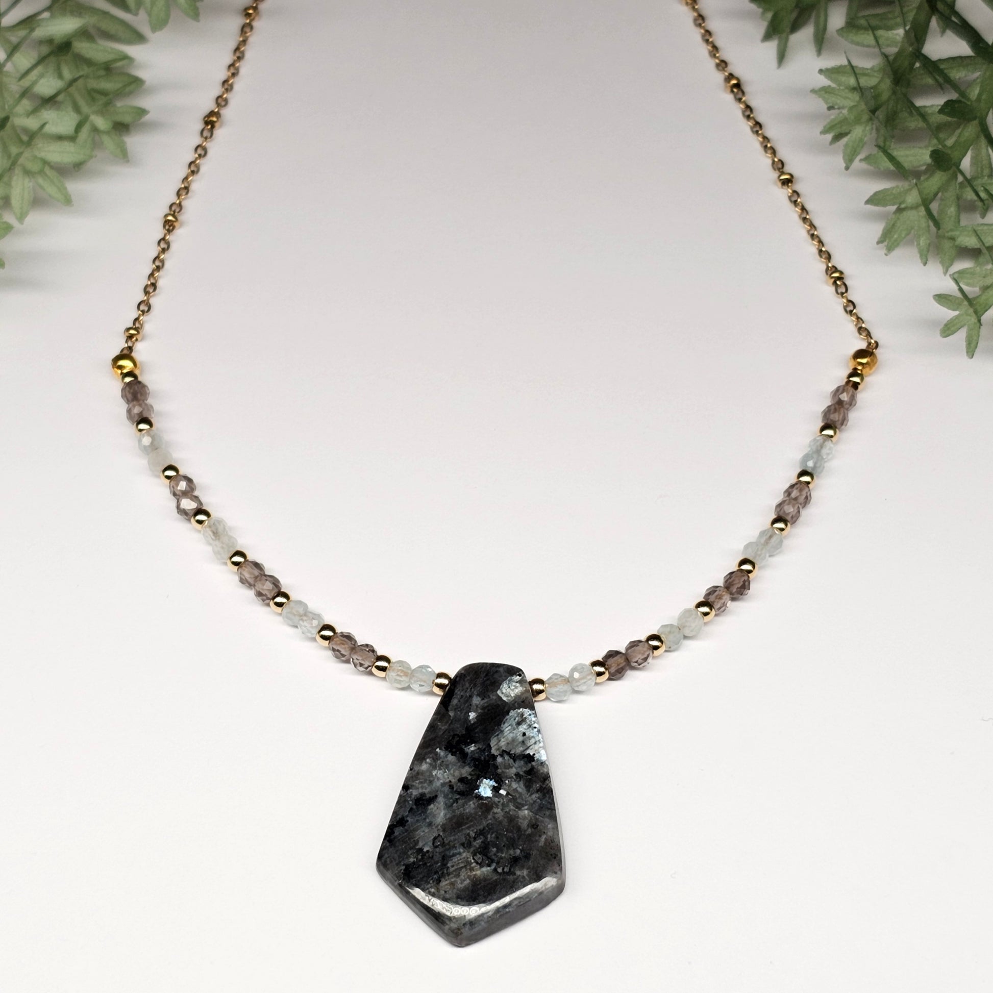 Lunar bloom is a focal Larvikite pendant necklace adorned with Smoky Quartz and Aquamarine beads.